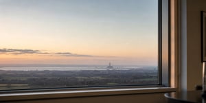 Calm dusk view of a distant UK infrastructure horizon through a modern office window, in muted tones