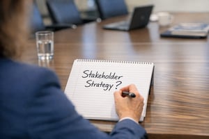 person sitting in a meeting room, wrtiting 'stakeholder strategy?' in a piece of paper